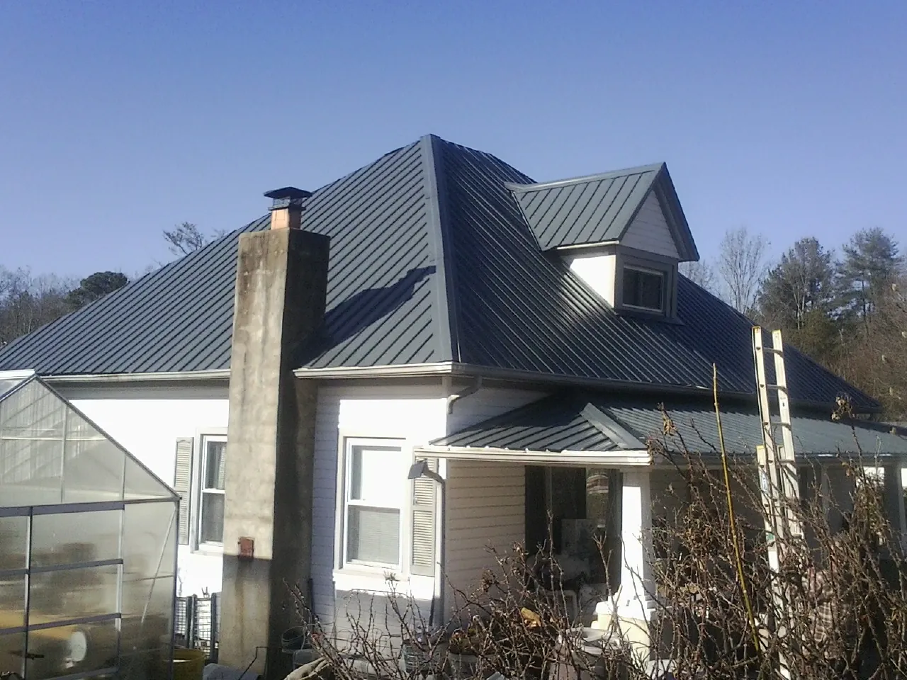 Dark blue standing seam metal roof on a white farmhouse with dormer in Elwood